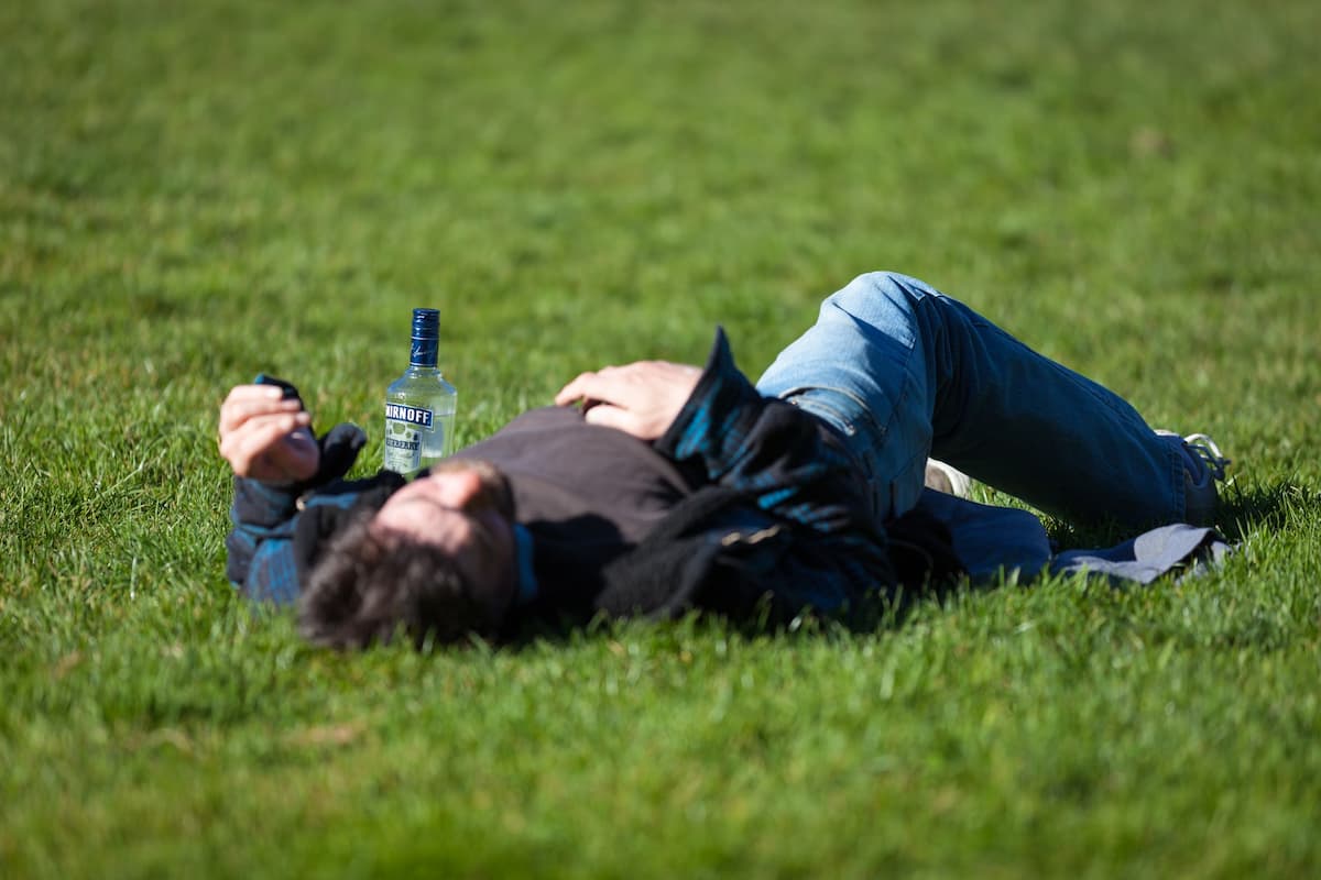 Alcoolique évanoui dans l'herbe, une bouteille de vodka posée à côté